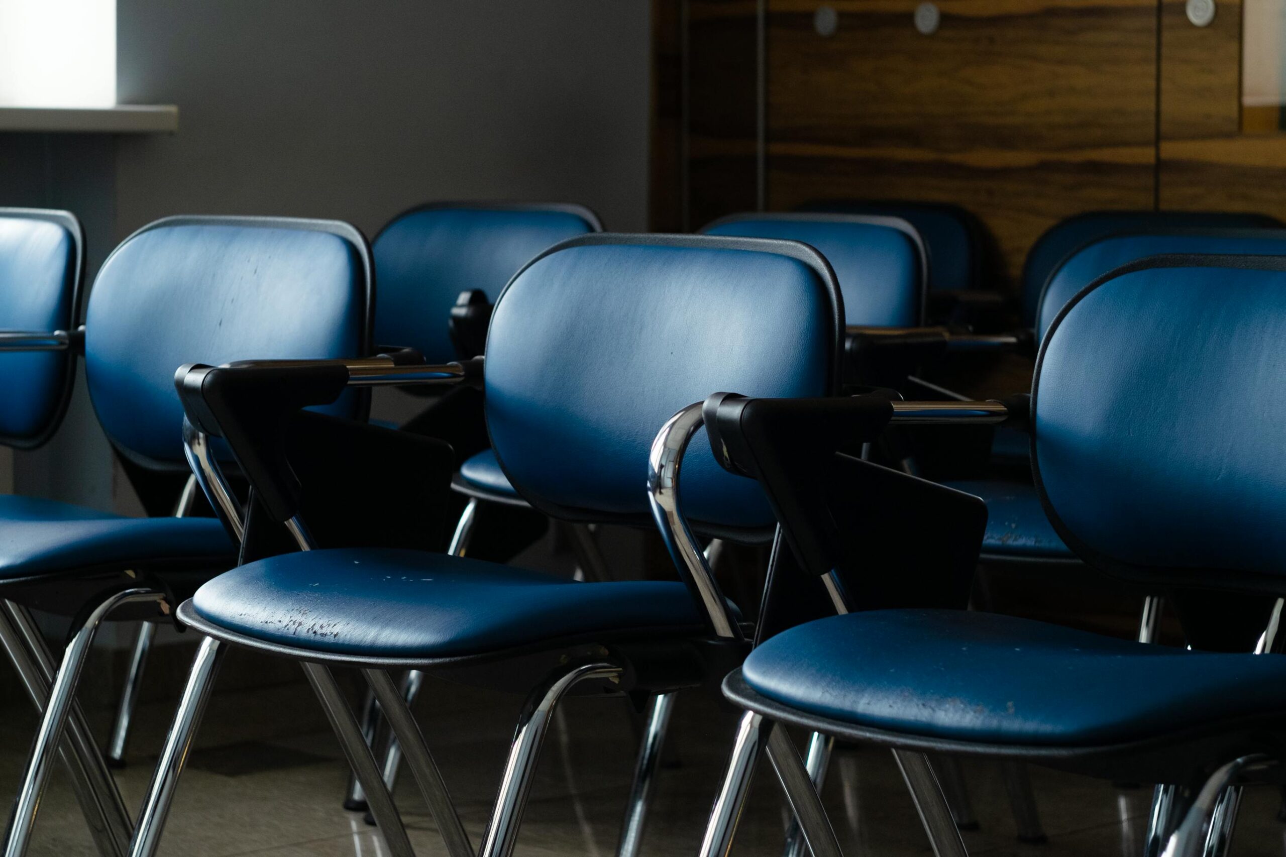 A row of blue desk chairs in a quiet, dimly lit room, ready for use.