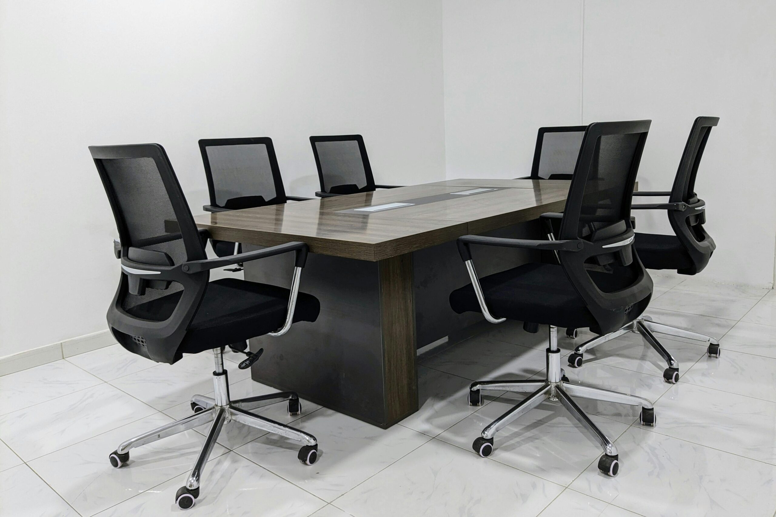 A neat and minimalistic conference room setup with black mesh chairs around a dark wooden table.