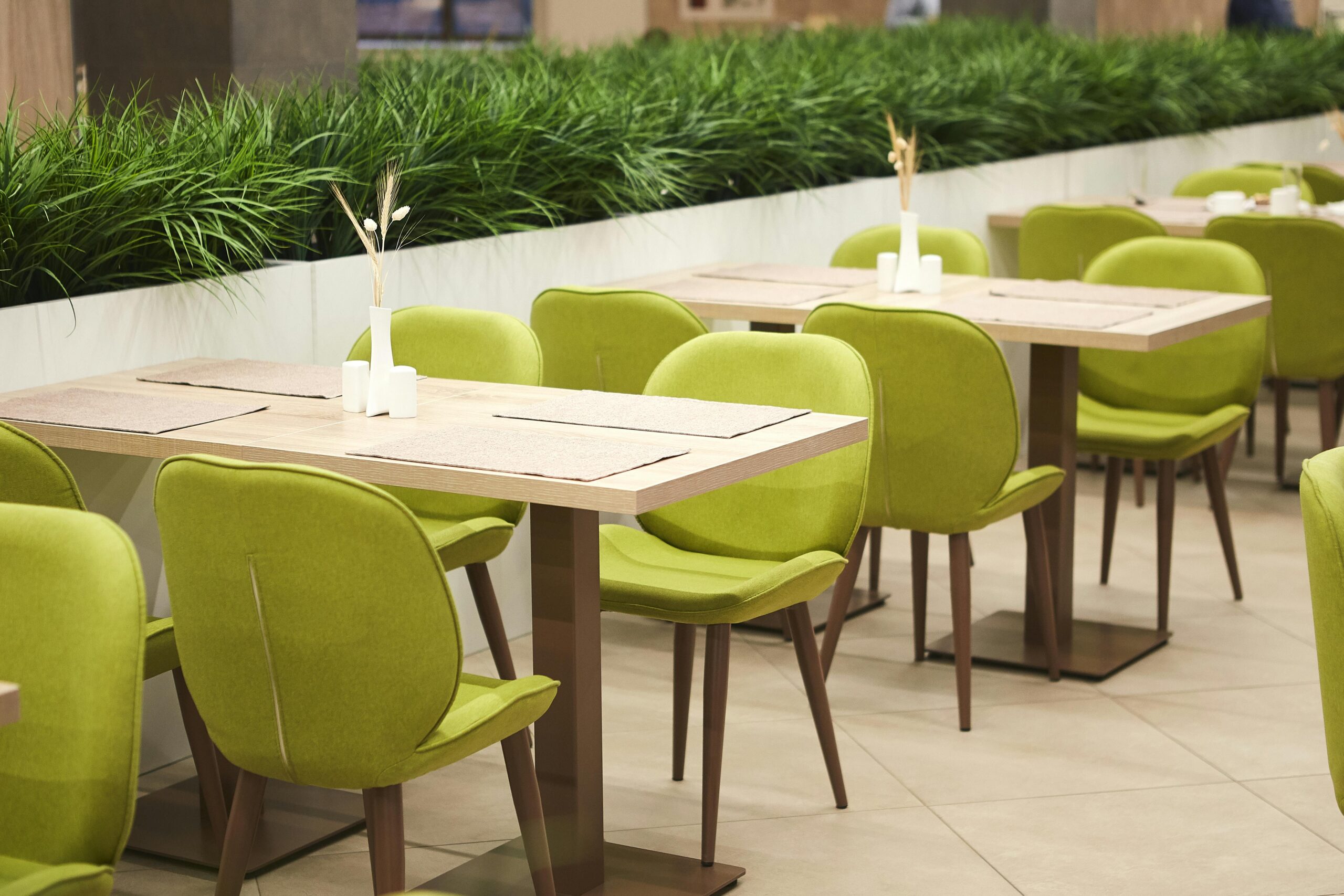 Contemporary dining area with green chairs and wooden tables indoors.
